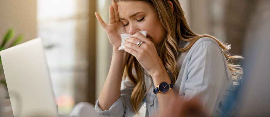 Young businesswoman with clpd and flu virus blowing nose while working in the office.